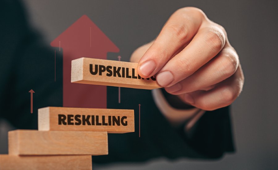A hand places a wooden block labeled "UPSKILLING" on top of a stack of blocks, with the top block below it labeled "RESKILLING." Red upward arrows are superimposed, indicating growth and progression.
